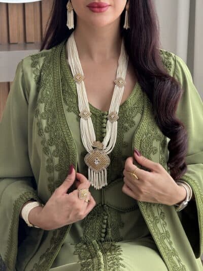 Elegant woman wearing traditional green embroidered dress and luxurious jewelry from Taj Almaha.