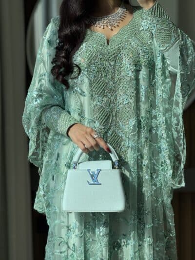 Elegant traditional green embroidered dress with jewelry and designer handbag for special occasion.