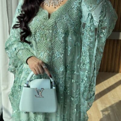 Elegant turquoise embroidered traditional dress with intricate beadwork and embellishments, paired with a stylish white handbag.