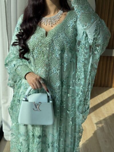 Elegant turquoise embroidered traditional dress with intricate beadwork and embellishments, paired with a stylish white handbag.