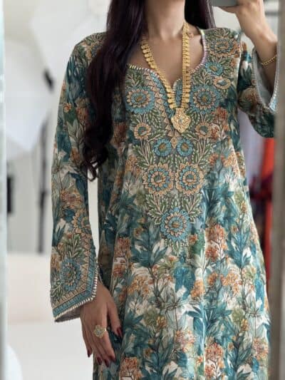 Vibrant floral embroidered traditional dress with gold jewelry for special occasions.