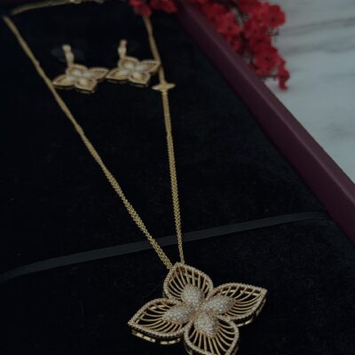 Gold butterfly pendant necklace and matching earrings with diamond accents on black velvet display.