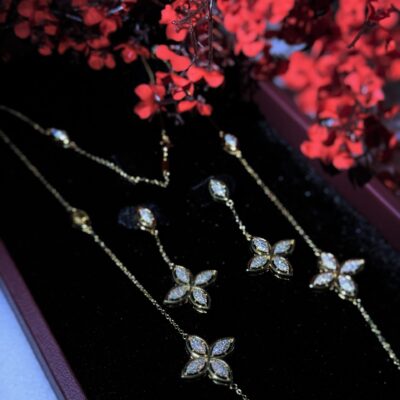 Elegant gold jewelry set with diamond-encrusted floral designs, beautifully displayed with vibrant red flowers.