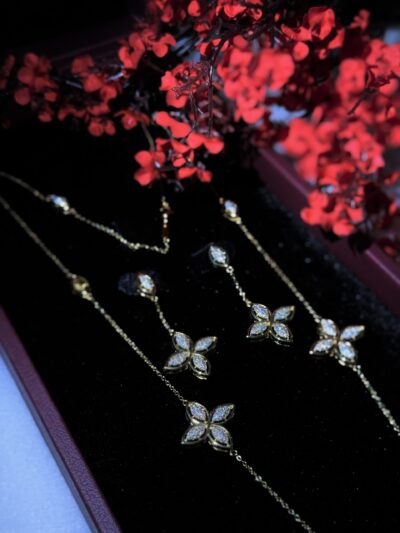 Elegant gold jewelry set with diamond-encrusted floral designs, beautifully displayed with vibrant red flowers.