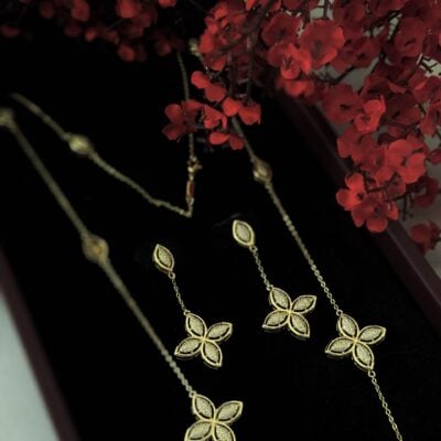 Elegant gold jewelry set featuring floral designs, showcased with red flowers for luxurious appeal.