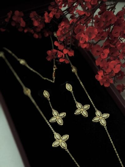 Elegant gold jewelry set featuring floral designs, showcased with red flowers for luxurious appeal.