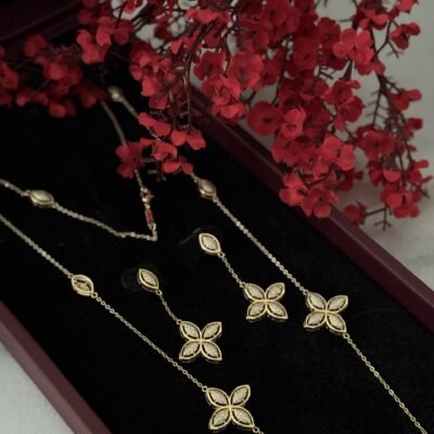 Elegant gold jewelry set with butterfly motifs displayed on black velvet, complemented by vibrant red flowers.