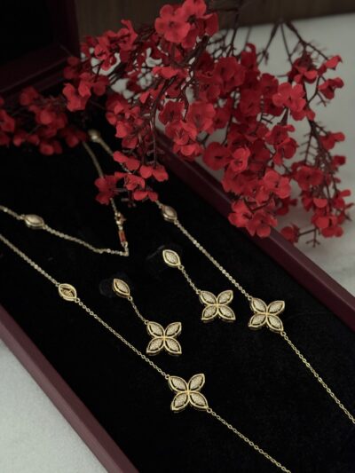 Elegant gold jewelry set with butterfly motifs displayed on black velvet, complemented by vibrant red flowers.