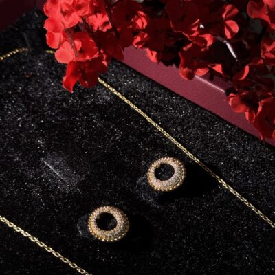 Elegant gold jewelry with sparkling circular earrings and delicate chain on black velvet background.