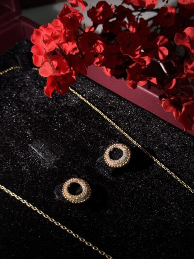Elegant gold jewelry with sparkling circular earrings and delicate chain on black velvet background.