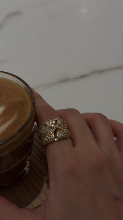 Gold and diamond ring on finger near a cup of coffee, luxury jewelry, elegant accessory, TAJ ALMAHA.